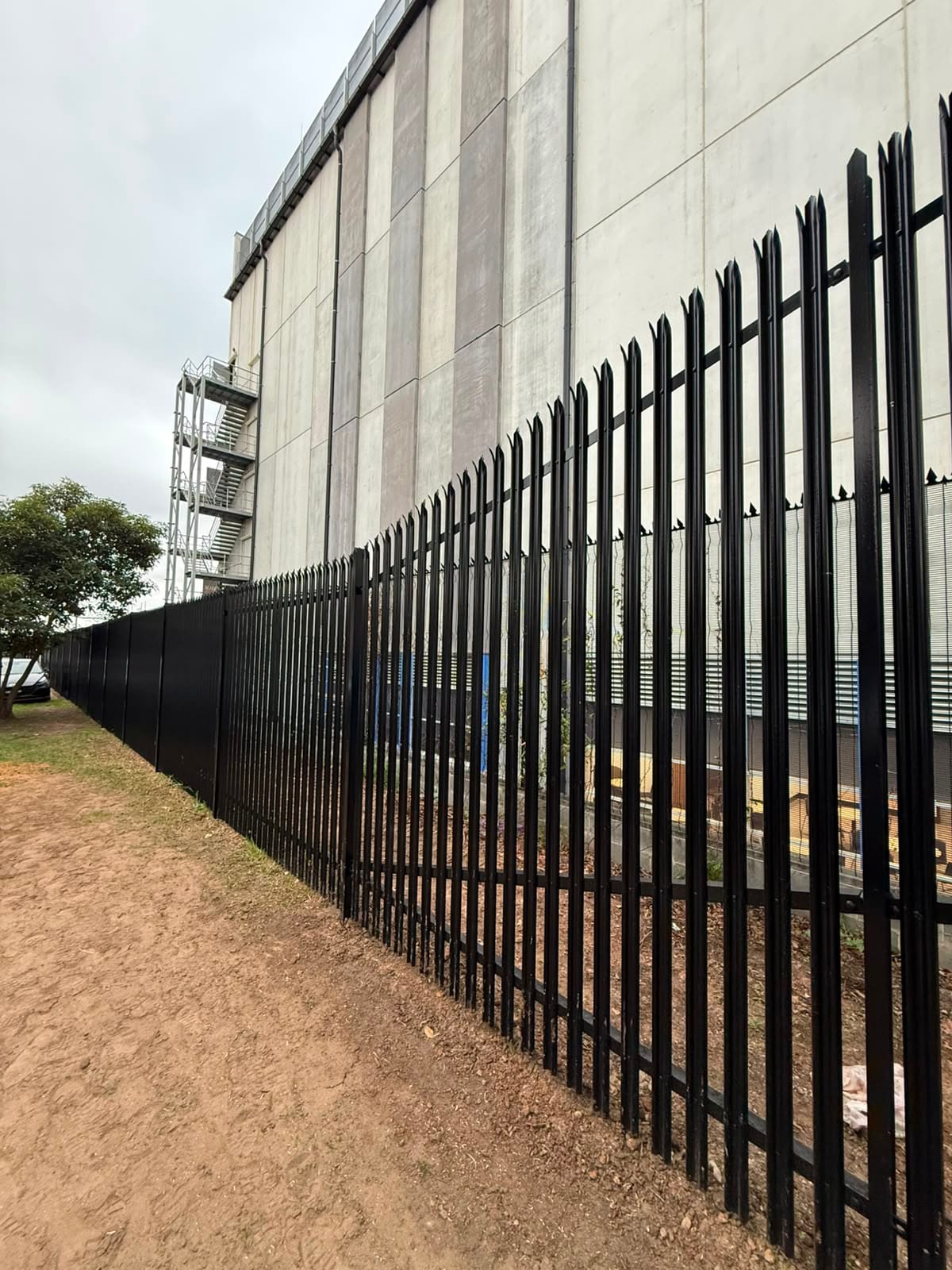 Black powder coated palisade perimeter on a plant boundary, June 2026